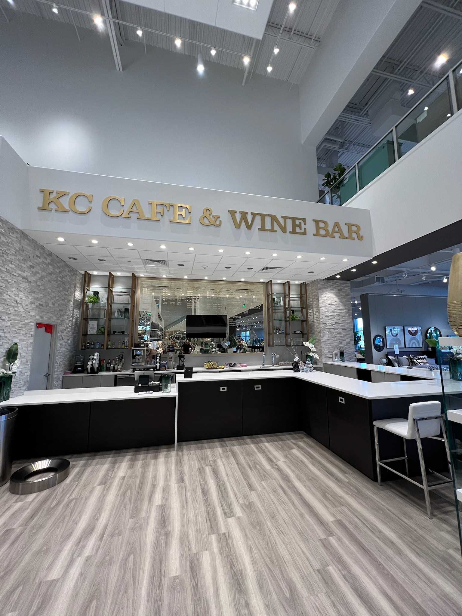 Commercial cafeteria bar with dark wood cabinetry, white countertops, textured gray stone accent walls, and gold signage.