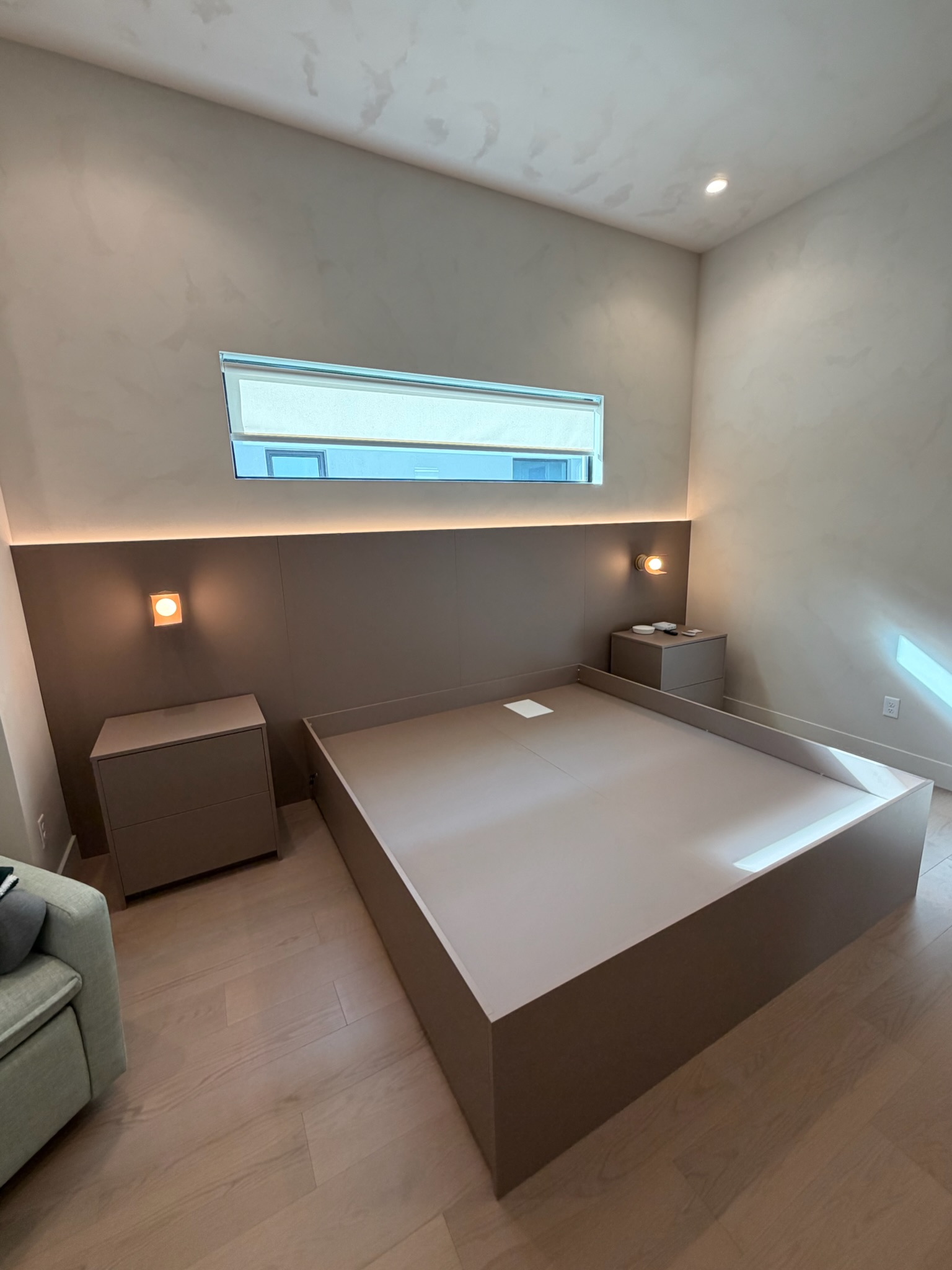 Taupe custom millwork bed with integrated nightstands and wall panels in a modern bedroom with cove lighting.