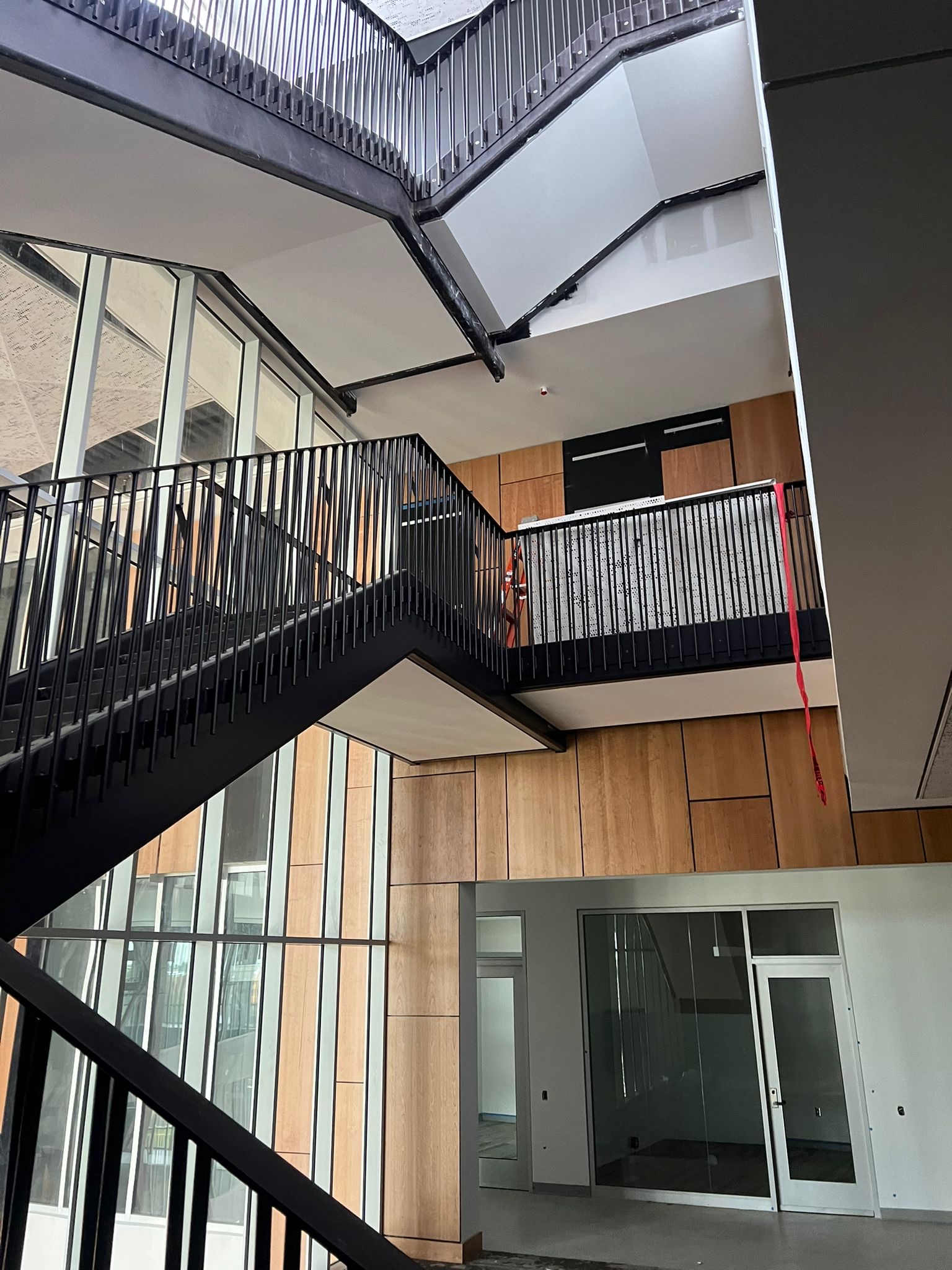 Multi-level commercial interior featuring black metal stairs, light wood paneling, and large windows.
