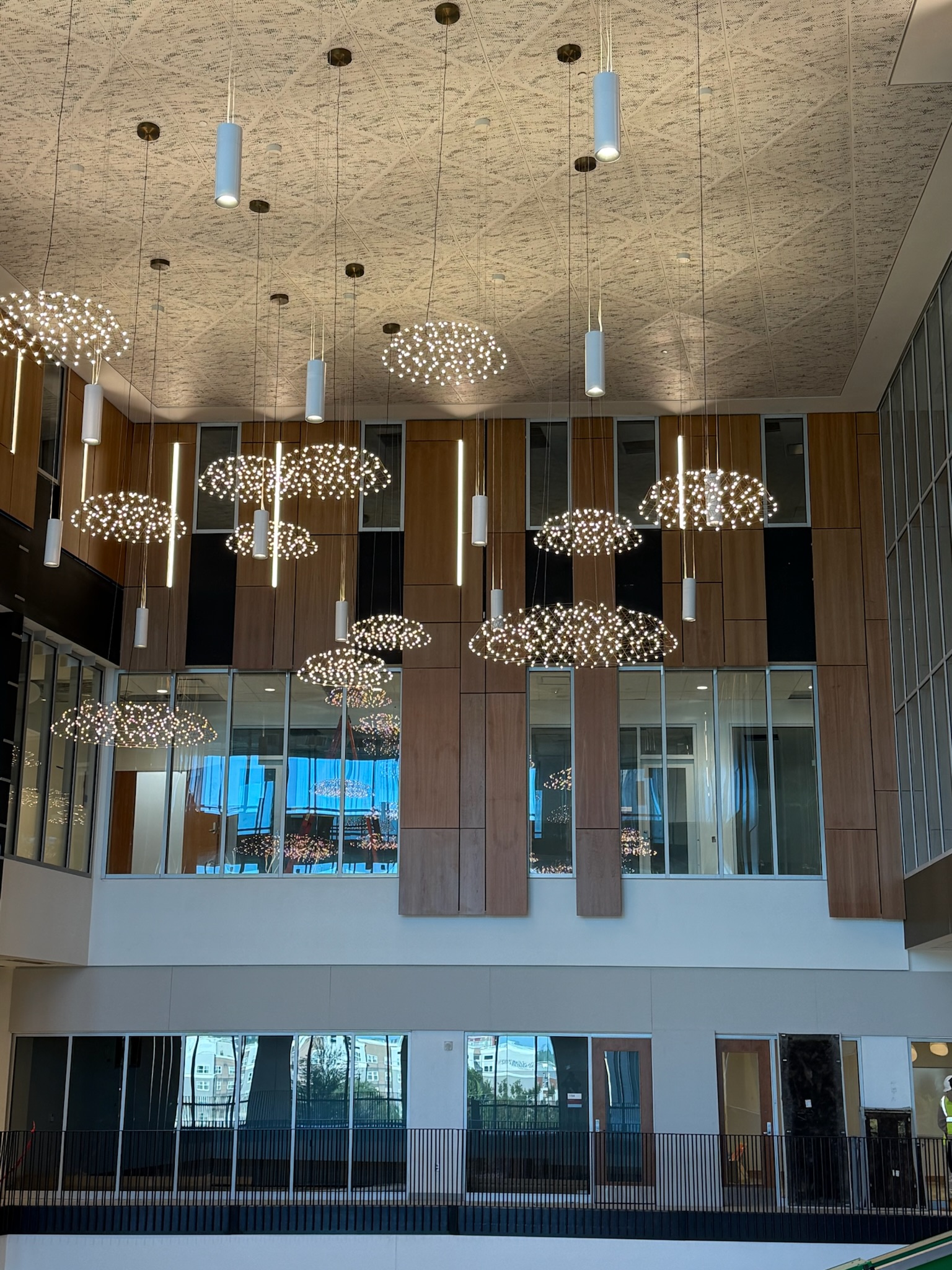 University atrium with wood wall panels, acoustic ceiling, and decorative pendant light fixtures.