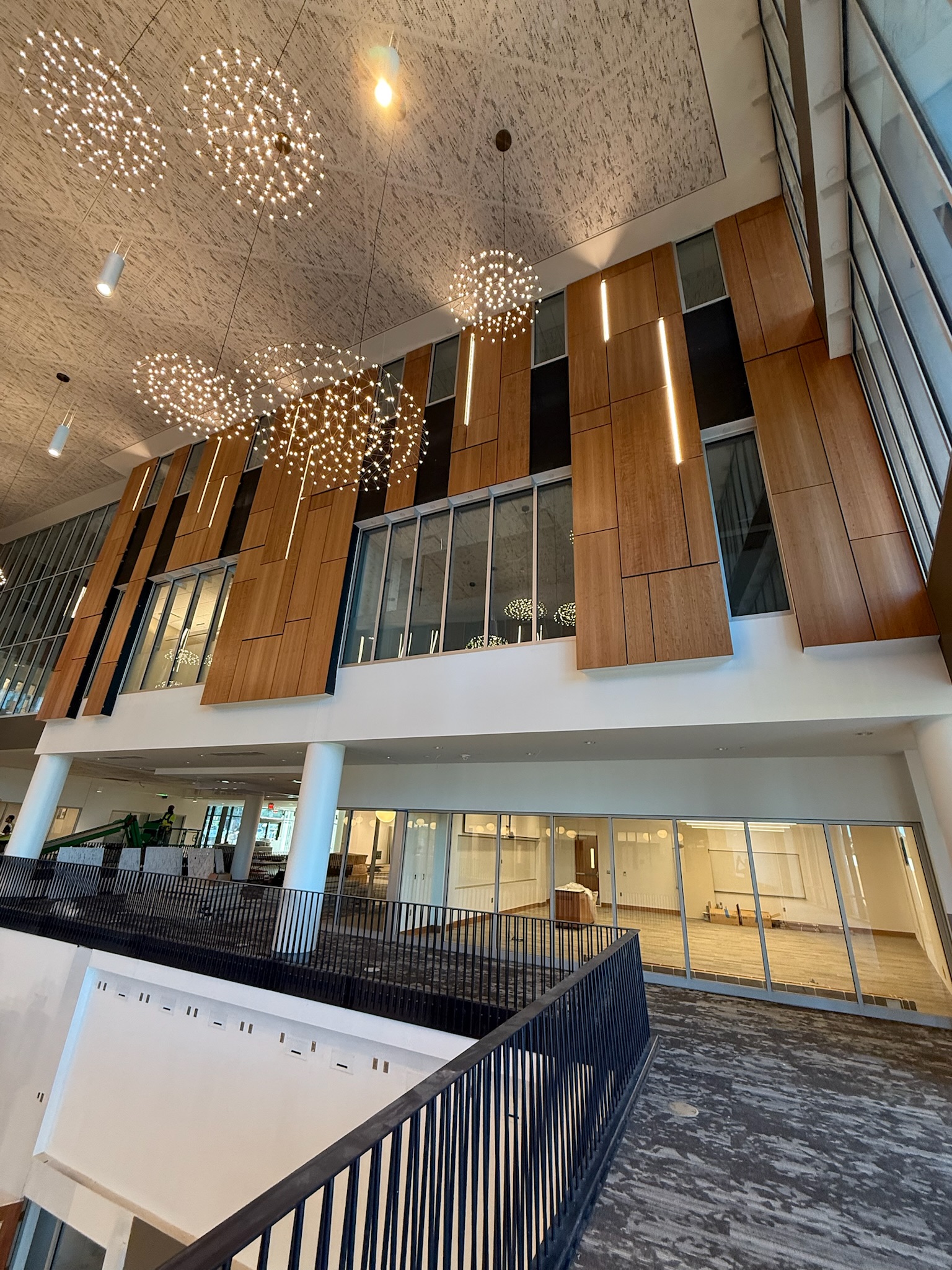 University atrium with walnut millwork panels, integrated linear LED lighting, and large spherical chandeliers.