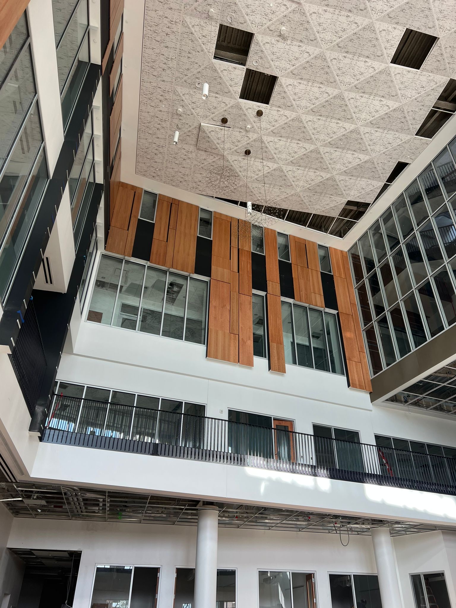 Multi-story atrium with wood paneling, black metal railings, and white walls, featuring a patterned acoustic ceiling.