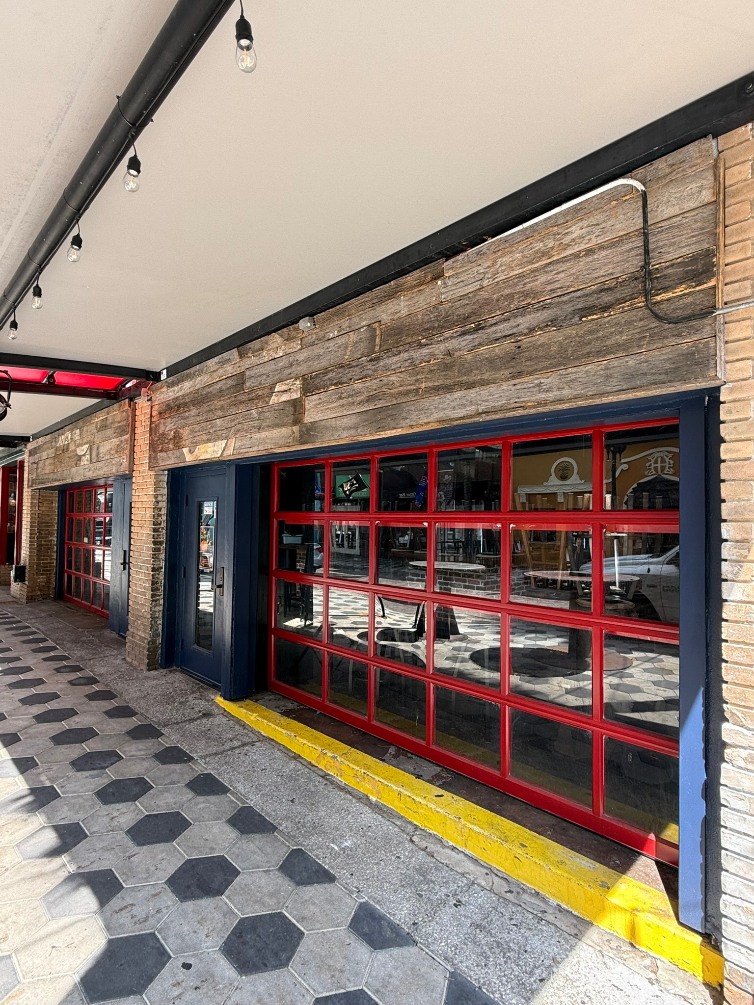 Exterior view of commercial building with reclaimed wood paneling, red and blue roll-up garage doors, and brick columns.