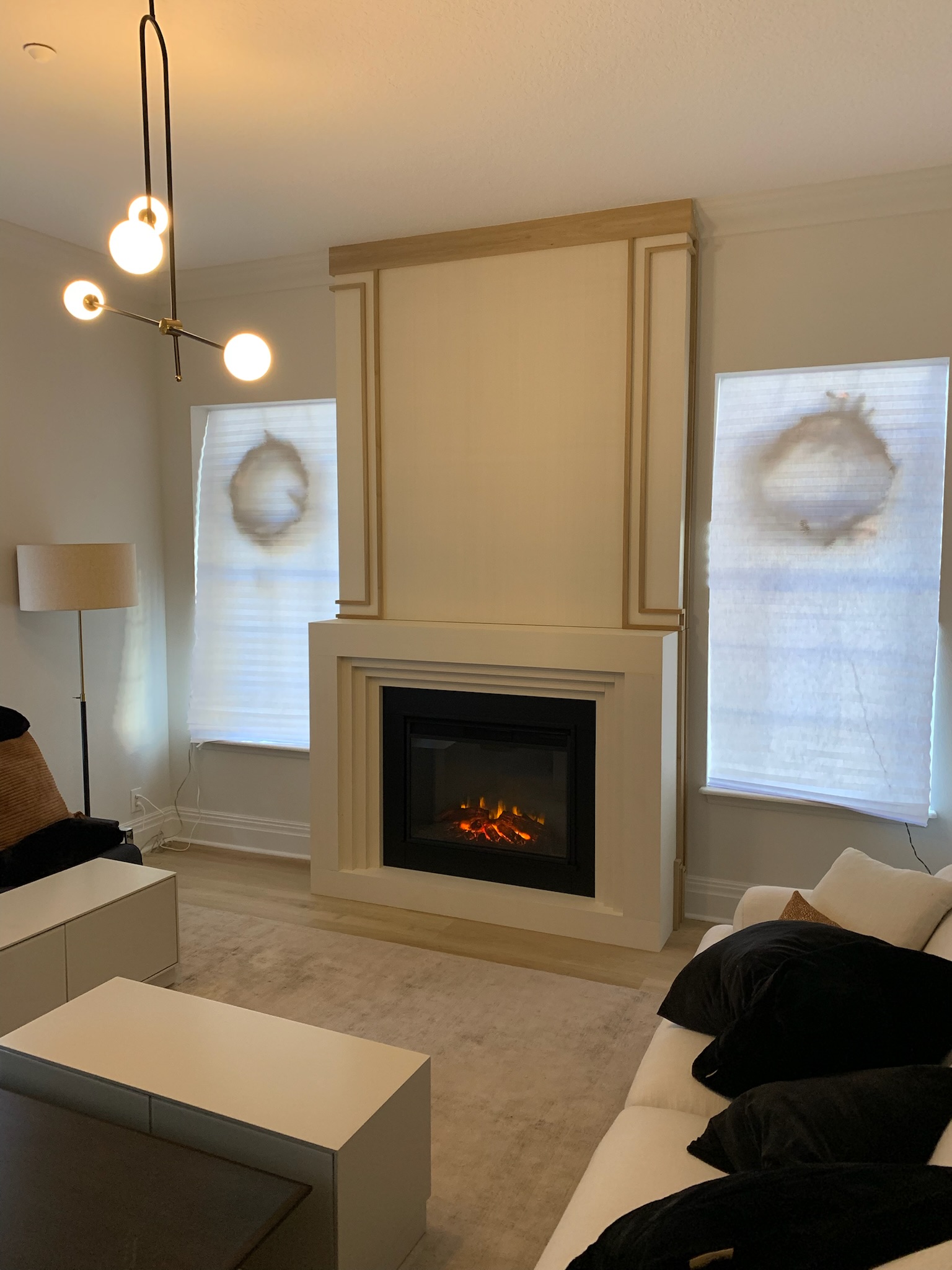 Formal living room featuring a fireplace with stacked surround millwork, light stained wood trim, and cream painted panels.