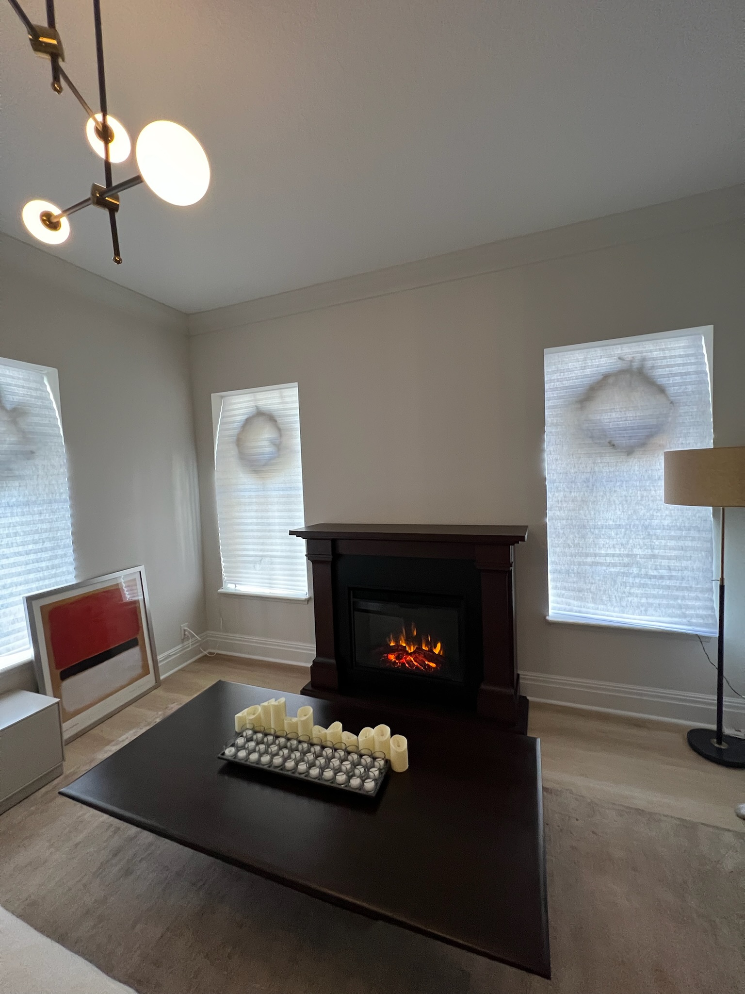 Formal living room with electric fireplace in dark wood mantel, contemporary chandelier, and large coffee table.