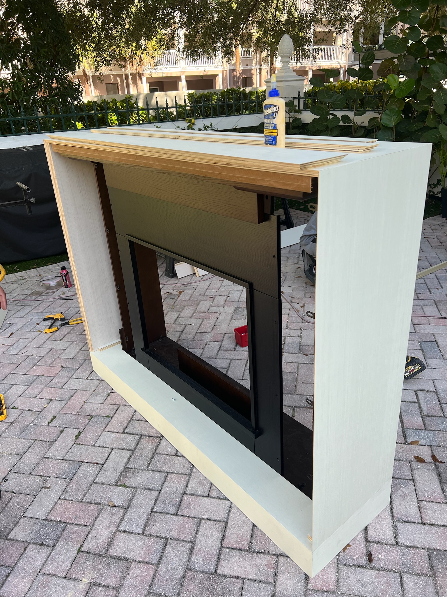 Unfinished custom millwork cabinet being assembled outdoors, showcasing raw wood, white-washed plywood, and integrated fireplace box.