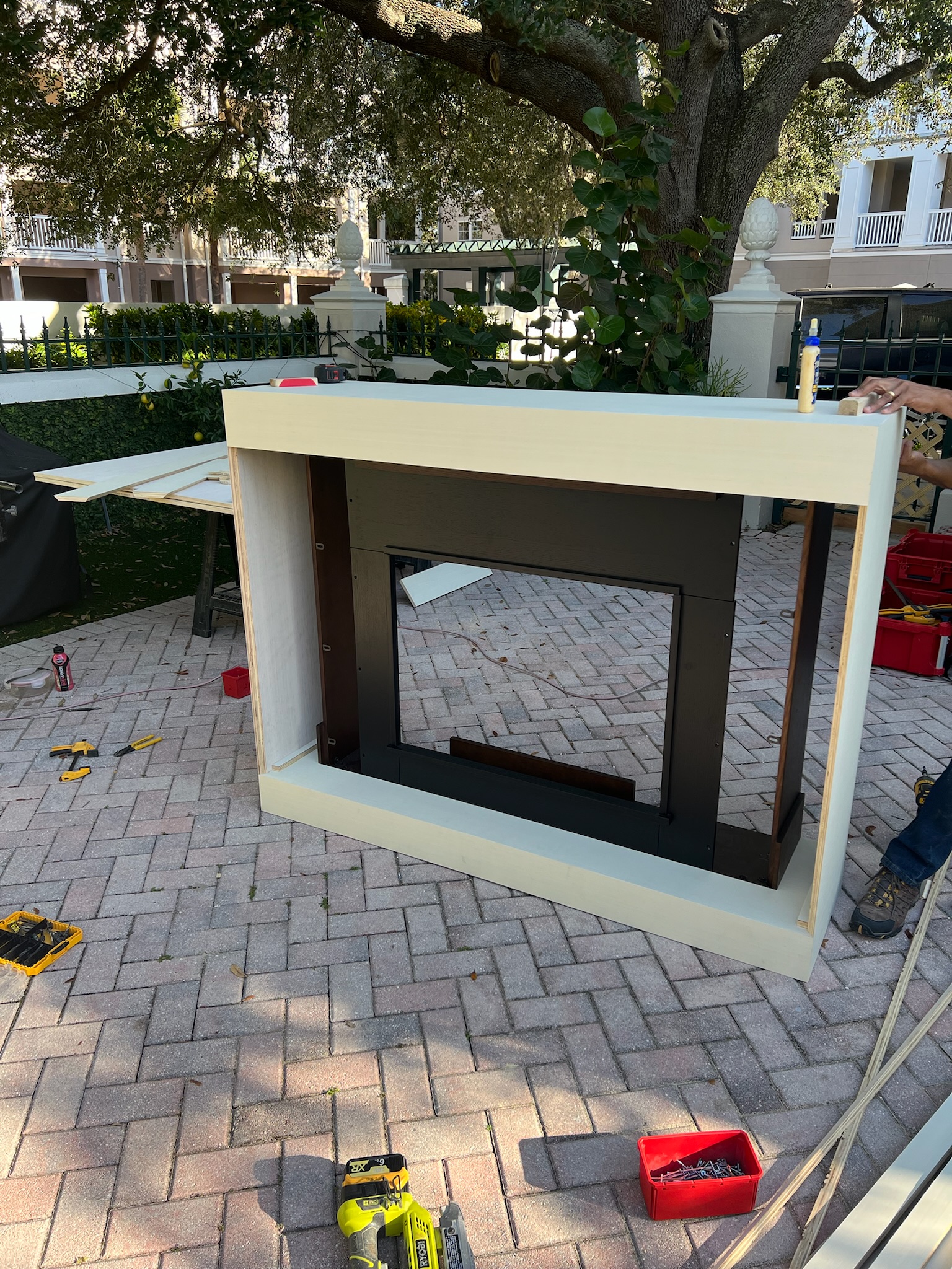 Unfinished custom fireplace millwork in pale white and dark brown being assembled outdoors on a brick patio.